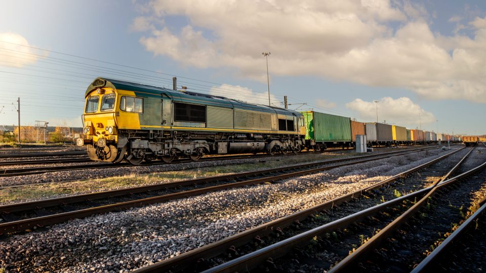 Profile view of a goods train with Intermodal wagons full of shipping container boxes for import and export in a yard or sidings