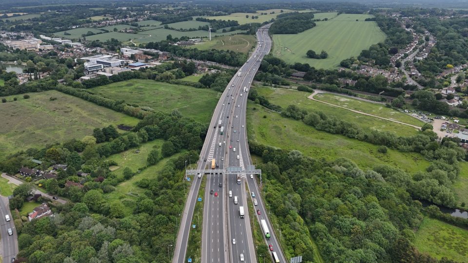 An aerial view of the bustling A41 and M25 motorway interchange in London, England, surrounded by green fields and residential neighborhoods.