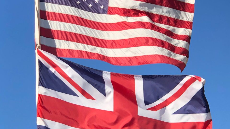 The American Flag and Union Flag on the same flag pole waving on the air in blue sky. Vertical shot