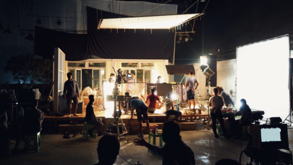 Blurry image of making movie video in big production studio and film crew team shooting or recording by professional digital camera and lighting set equipment.