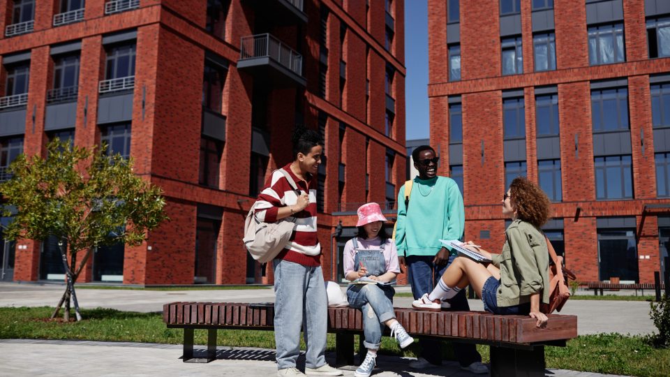 Wide angle view at diverse group of students studying together outdoors in urban setting at modern college campus, copy space
